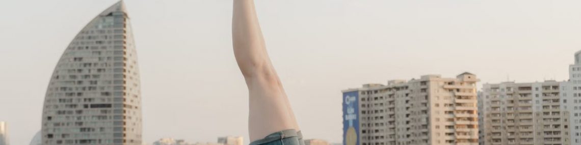 Woman lying on rooftop edge with leg raised against urban city backdrop during daytime.